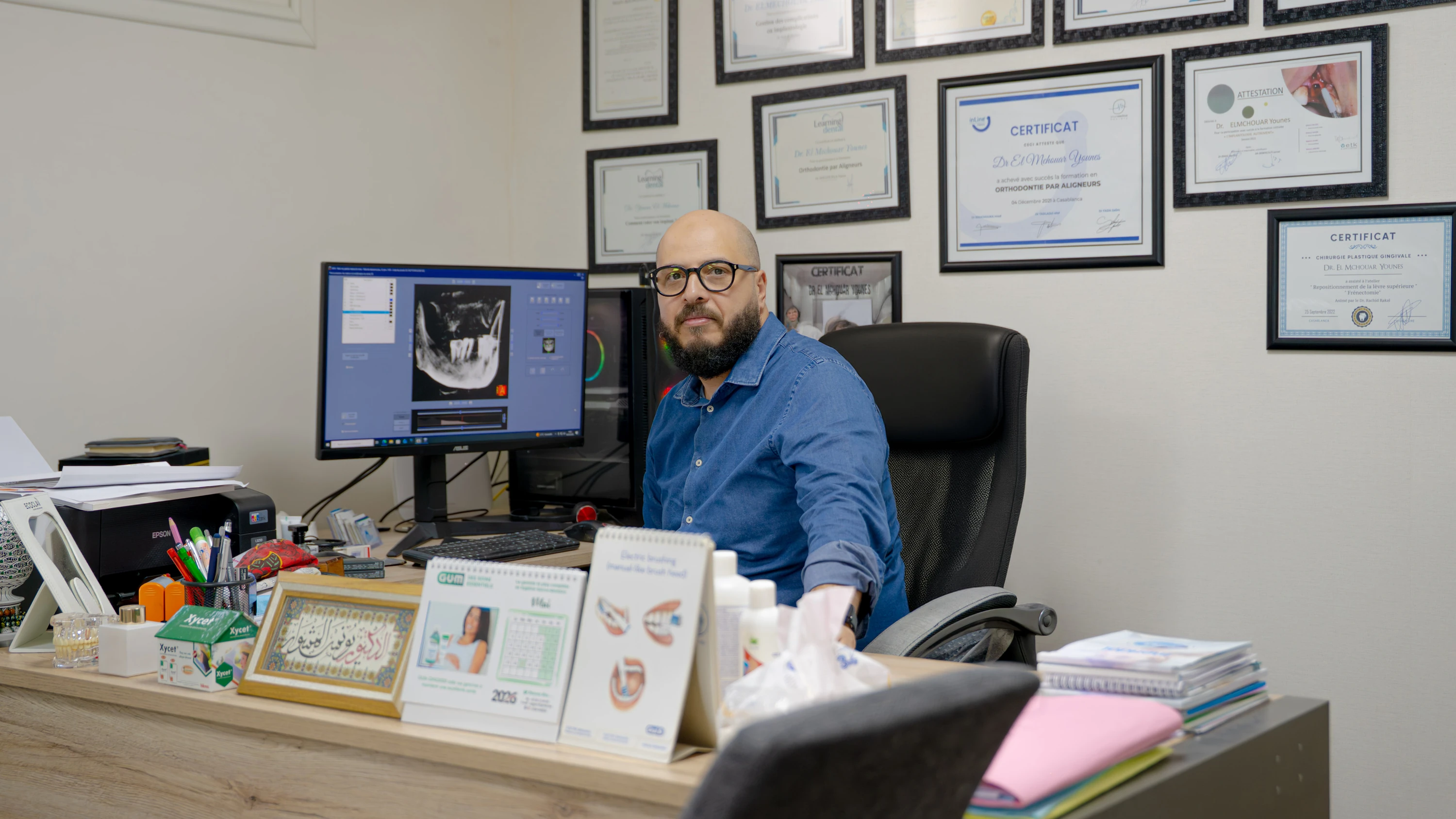 Dr Younes El Mchouar, chirurgien-dentiste à son bureau devant ses diplômes